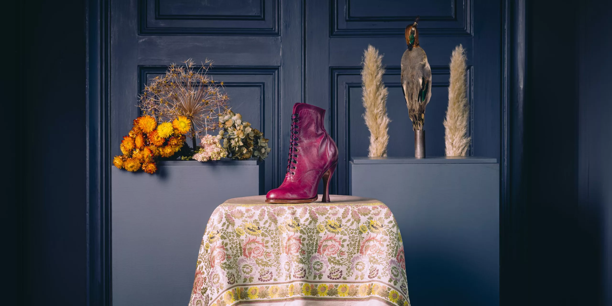 Oxford Bootie Pink lace-up boot displayed on an embroidered chair beside flowers