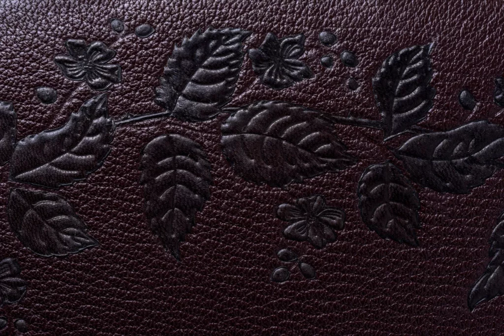 Fine leaf and berry details embossed onto a luxurious deep brown leather. A close up photo of an exquisite clutch case by Caroline Groves