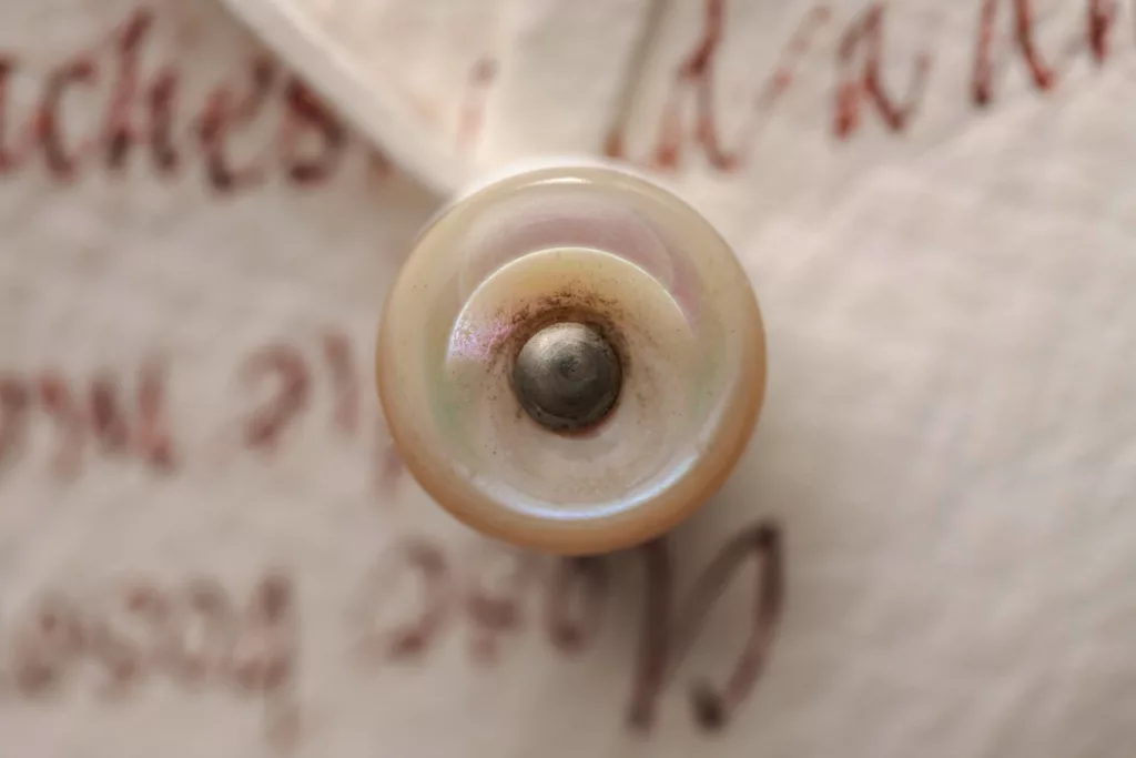 Close up of the button on an alum tawed leather shoe, with a bellows tongue featuring hand scribed calligraphy. Taking the lines from inspiring poems of Keats. The heel is a classic Caroline Groves curvaceous shape, leather covered and with an oak bark leather top piece and sole. A single button fastens the shoe and linings and all natural giving simplicity and focus on the calligraphy.