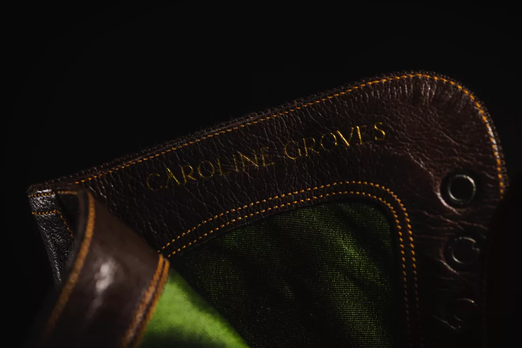 The close up of the top of an Oxford bootie by Caroline Groves. Here you see the stunning green silk lining within the chestnut brown leather lace up. The Caroline Groves name is also revealed in gold foil along side metal eyelets and a burnt orange stitch.