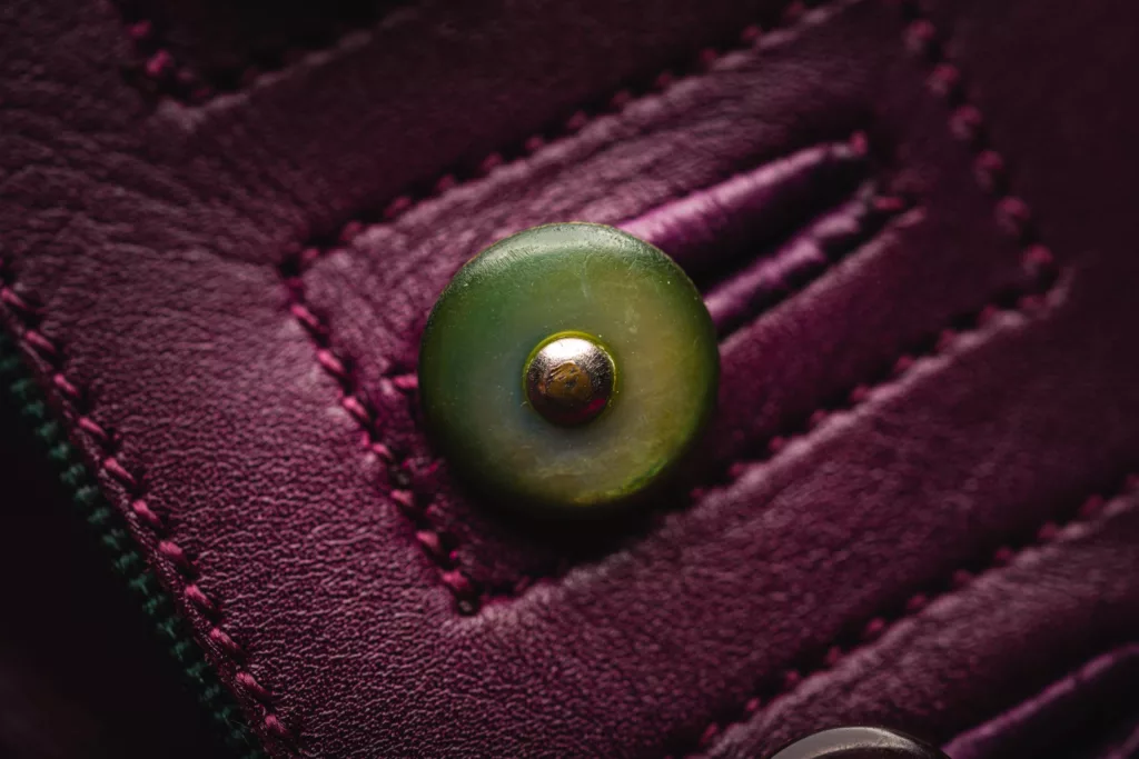 Close up on a vintage button on this wonderful button shoe in vibrant magenta polished calf leather. With 3 Button fastenings on each foot, the main detail of this pair is upon its heel. The block heel showcase a fine work of silk embroidery, depicting an exotic bird in flight. The bright rich colours of the silk embroidery make this an exception piece of art. The shoe has a hand sewn welt and hand stitched oak bark tanned sole.