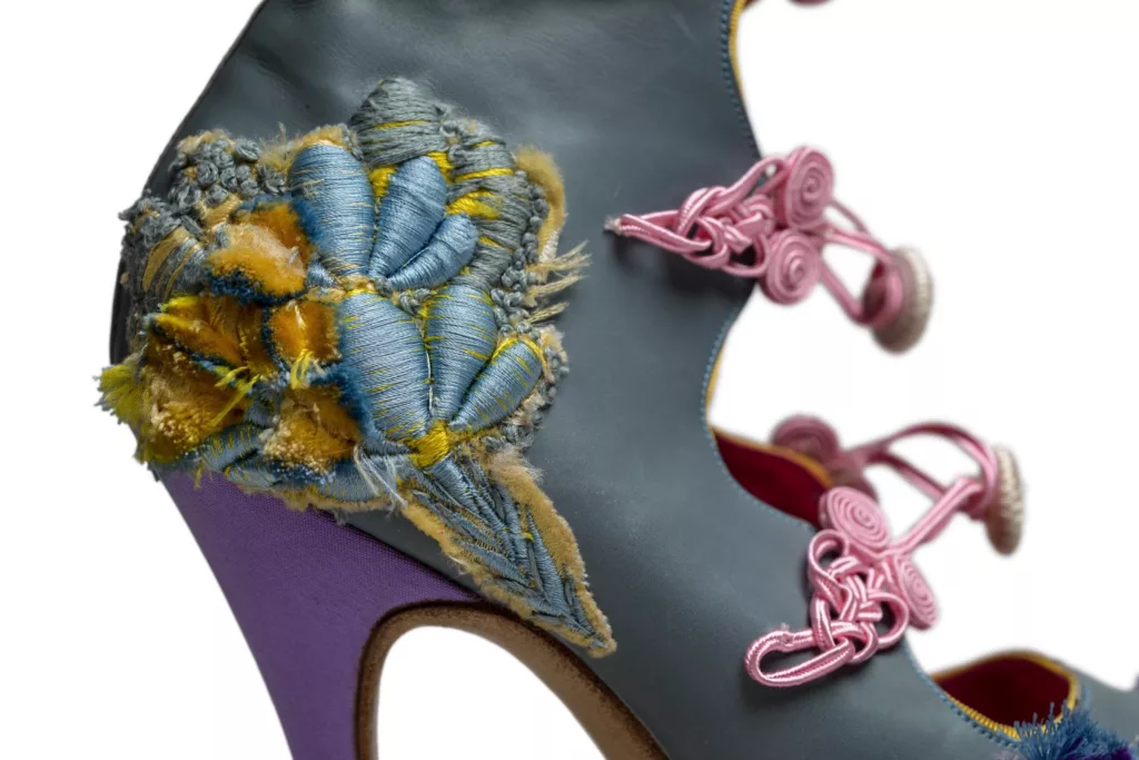 An open toe, open fronted boot with frogging closures. In pale blue baby calf with covered platforms and heels of vintage French silk in mauve. The ‘Exploding Flowers’ are worked in velvet embroidery of an array of pastel colours. Here is a close up of said exploding flowers in pale blue and yellow.