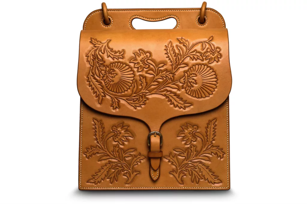 Full front photo of the Valerie oak bark tanned shoulder case bag. The fine detail of oak leaf inspired tooling onto the leather, creating shadows and depth to the piece. Featuring a fastening of brass and the detail of hand stitched linen thread. Curved shapes and clean cut raw edge leathers add to this striking design