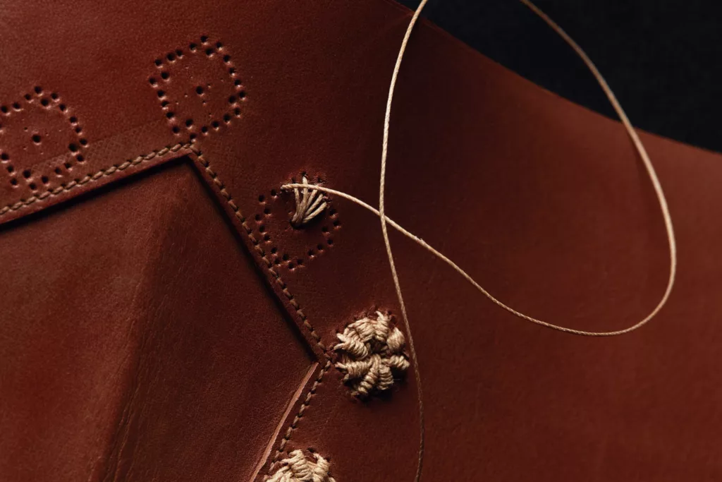 A close up on the hand worked embroidery on a vegetable tanned leather western style boot. A natural linen thread create a flower sort of adornment running along an edge of the boot.