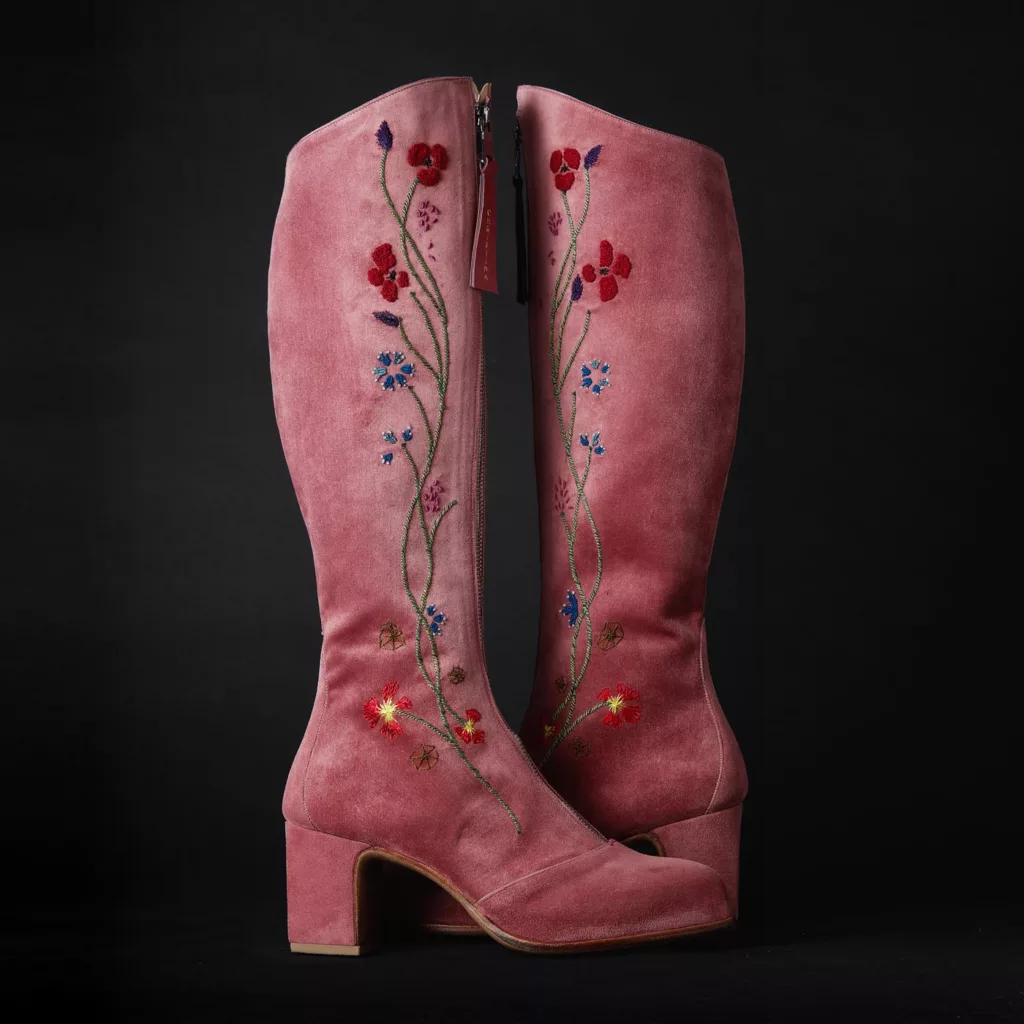 Long leg, zip front boot in dusky pink baby calf suede. The hand embroidery worked in silk thread features stylised yellow, red, blue and white flowers, green stems intertwined with rope-like strands. Oak bark tanned leather soles and top pieces.