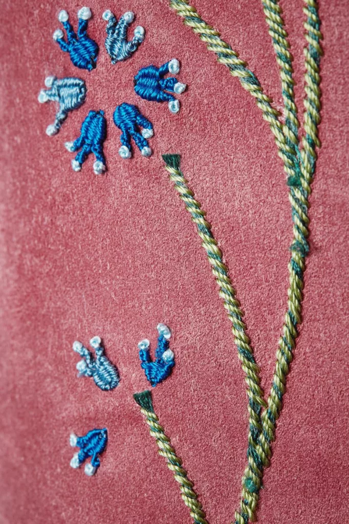 Long leg, zip front boot in dusky pink baby calf suede. The hand embroidery worked in silk thread features stylised yellow, red, blue and white flowers, green stems intertwined with rope-like strands. Oak bark tanned leather soles and top pieces.
