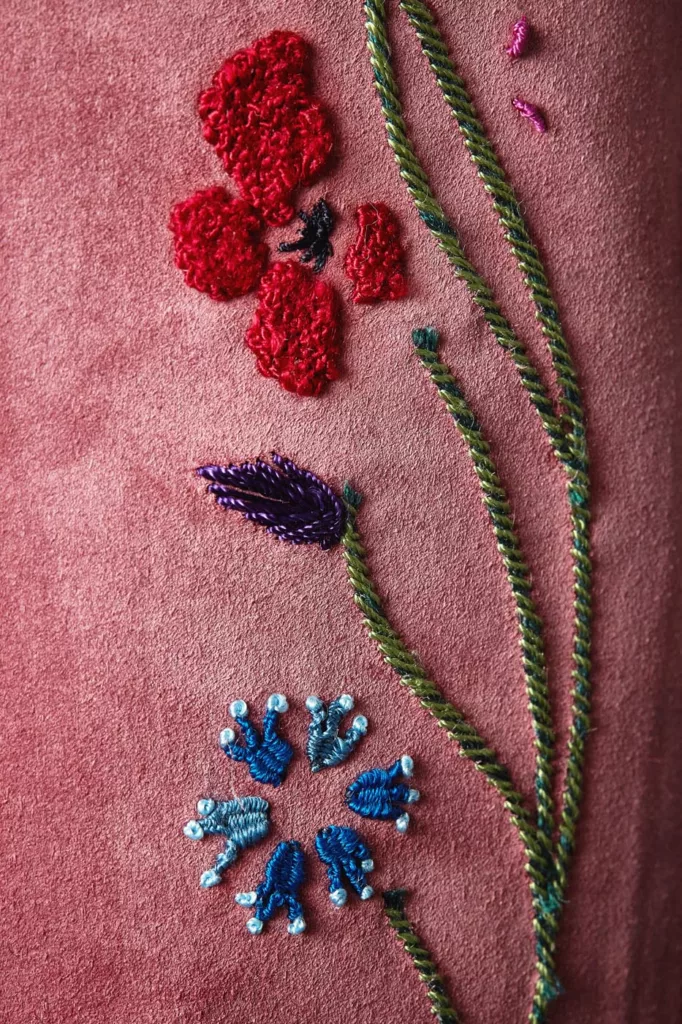 Long leg, zip front boot in dusky pink baby calf suede. The hand embroidery worked in silk thread features stylised yellow, red, blue and white flowers, green stems intertwined with rope-like strands. Oak bark tanned leather soles and top pieces.