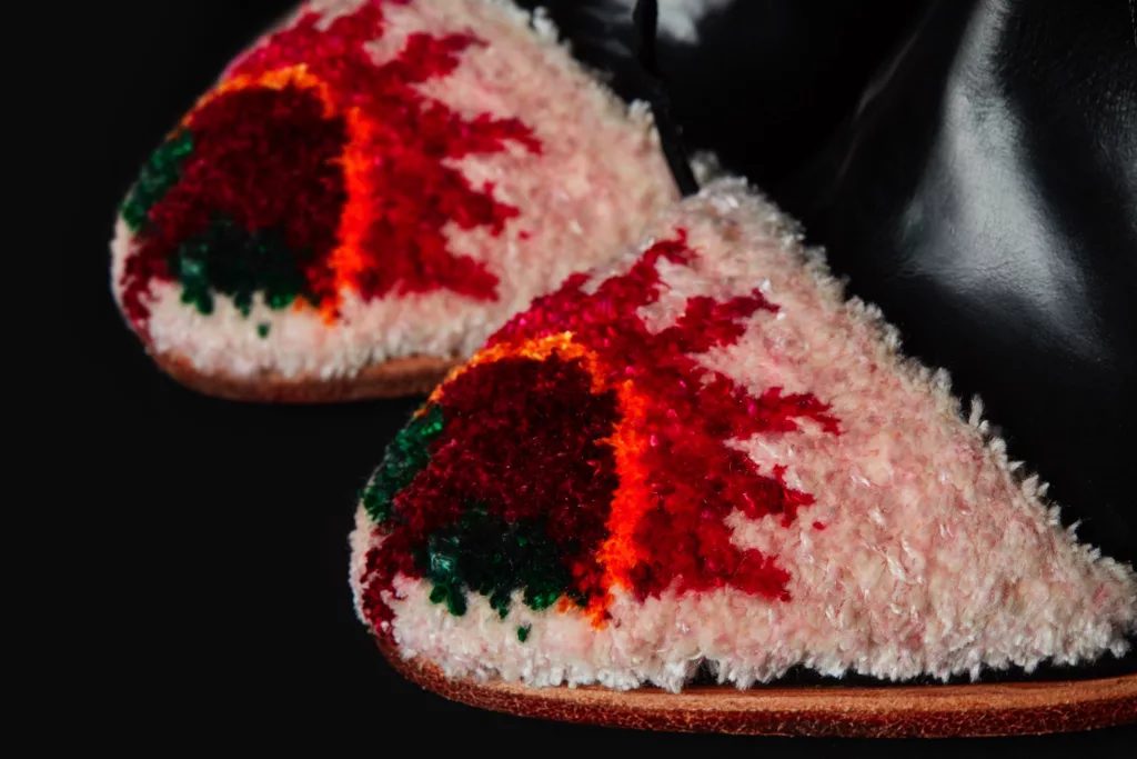 Close up of the intricately hand embroidered toe cap of a Caroline Groves Red Dawn high heeled George bootie. A striking embroidered detail in reds, orange, pink and deep green, all against the black polished leather of the bootie.