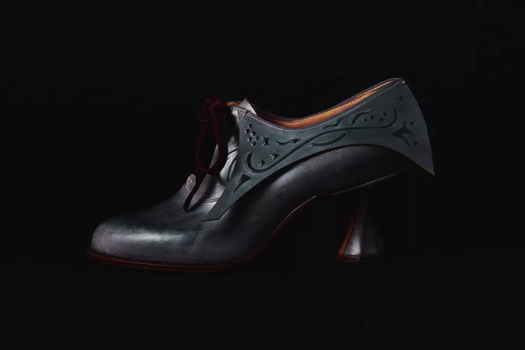 Side view of the balmoral shoe with embossed collar detail, inspired by pre Raphaelite paintings. A deep grey veg tanned leather with a contrasting ruby velvet ribbon lacing. This shoe is highly sophisticated with subtle and intricate details. Its heel is a geometric shaped Louis heel.