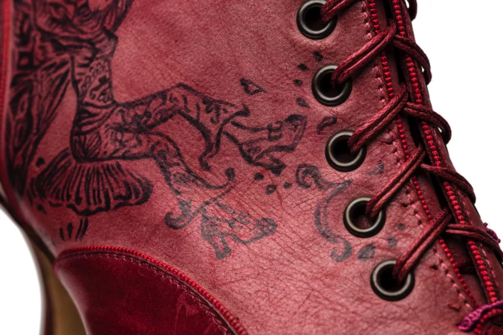 Hand inked art works on a luxurious ankle length lace up boot. Detailed , romantic lines make up fairy like figures and floral designs against a red leather