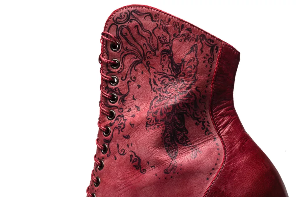 Hand inked art works on a luxurious ankle length lace up boot. Detailed , romantic lines make up fairy like figures and floral designs against a red leather