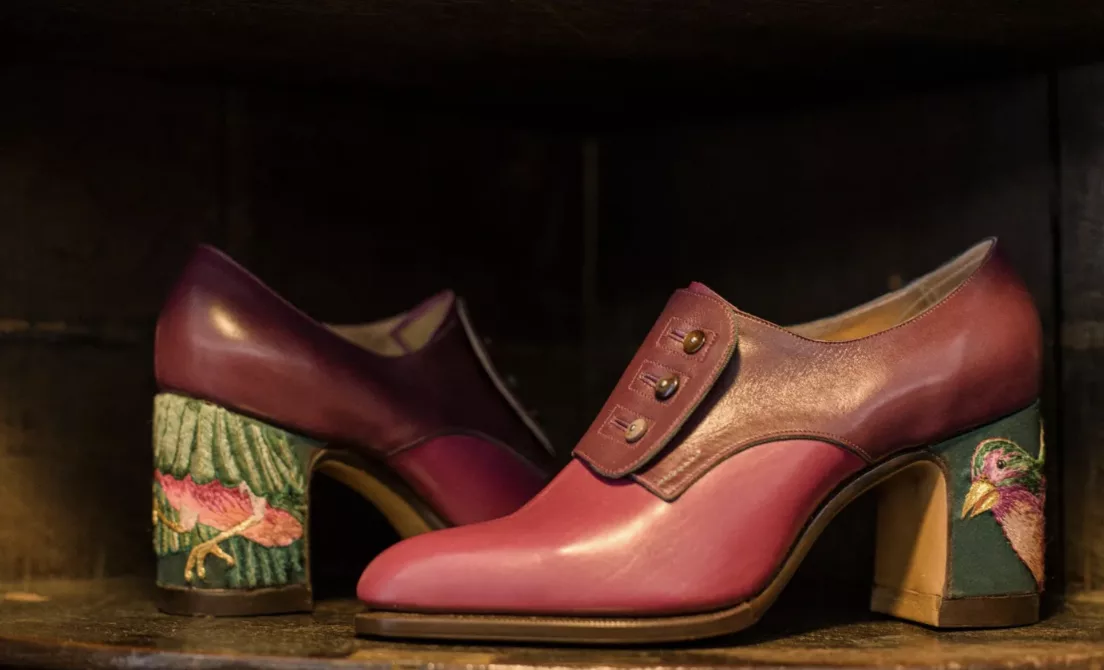 Black strap shoes with gold decoration arranged on a patterned yellow surface.